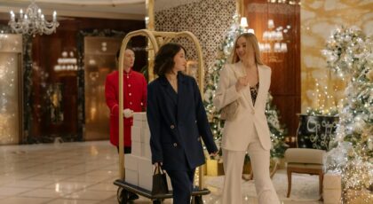 Two women in elegant suits walk through a decorated hotel lobby during festive winter season.