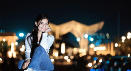 Portrait of a young woman smiling outdoors at night with city lights in the background.