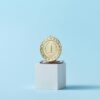 Close-up of a gold medal on a podium with a baby blue background, symbolizing victory.