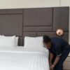 A hotel staff member prepares a bed in a sleek, modern hotel room with copper accents.