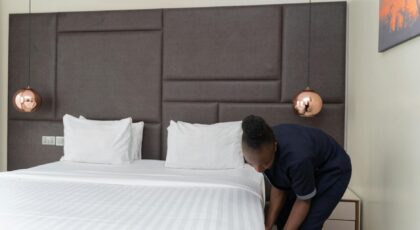 A hotel staff member prepares a bed in a sleek, modern hotel room with copper accents.