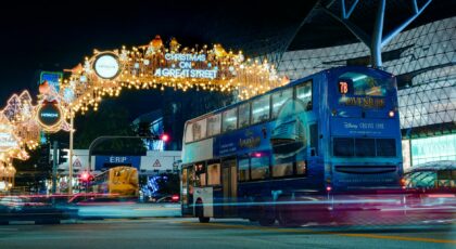 A vibrant night scene with a bus passing under festive Christmas lights on Orchard Road, Singapore.