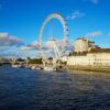 Iconic Ferris wheel London Eye over River Thames with bright blue sky.
