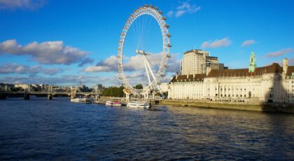 Iconic Ferris wheel London Eye over River Thames with bright blue sky.