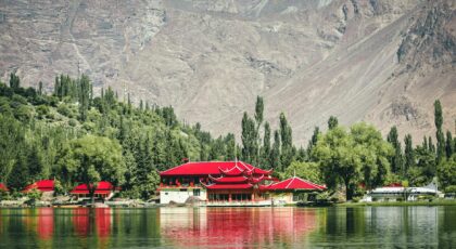 Stunning lake view with traditional architecture and vibrant red roofs framed by mountains and trees.