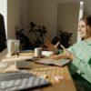 A woman in a green hoodie having a video call at her home office desk.