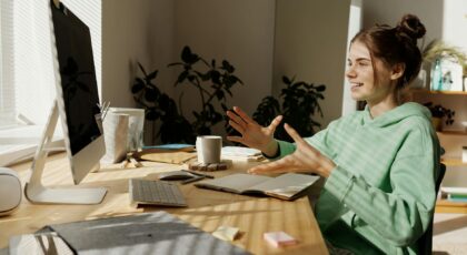 A woman in a green hoodie having a video call at her home office desk.