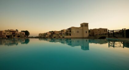 Elegant resort villas in Ras Al-Khaimah reflecting on tranquil water at dusk.
