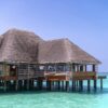 Stunning overwater bungalow with thatched roof on crystal-clear sea under bright blue sky, perfect for tropical vacations.