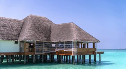 Stunning overwater bungalow with thatched roof on crystal-clear sea under bright blue sky, perfect for tropical vacations.