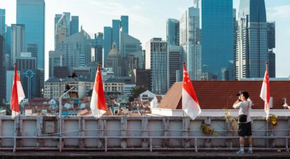 A photographer takes a picture of the Singapore skyline under a clear blue sky.