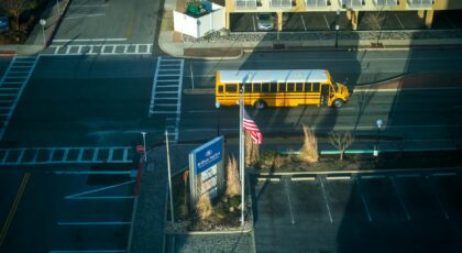 An aerial view of a yellow school bus driving through a quiet city street intersection next to a hotel.