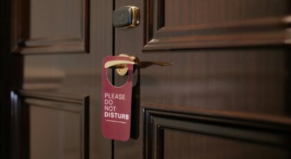 A wooden hotel door with a 'Please Do Not Disturb' sign hanging on the handle.