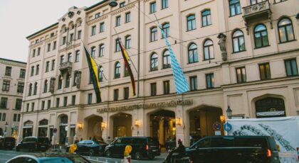 Street view of Hotel Vier Jahreszeiten Kempinski in Munich with flags and evening lighting.