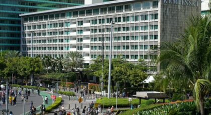 A vibrant view of the Kempinski Hotel in downtown Jakarta with people walking and cycling nearby.