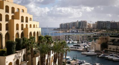 Scenic view of Hilton Malta's marina with yachts and palm trees, capturing urban luxury by the sea.