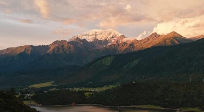Stunning landscape of a Tibetan village nestled below snow-capped mountains at sunset.