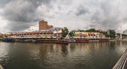 Panoramic view of Clarke Quay's colorful buildings along the Singapore River under a cloudy sky.